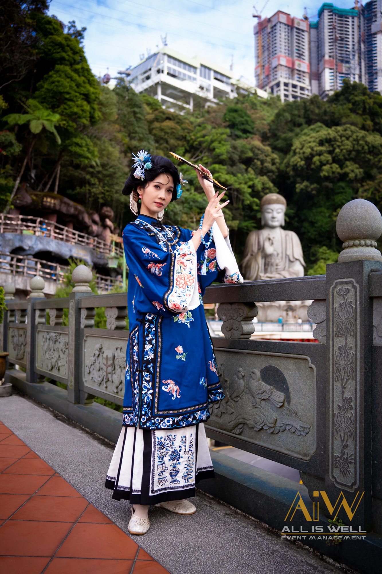 Portrait in blue traditional robe overlooking a city with a Buddha statue