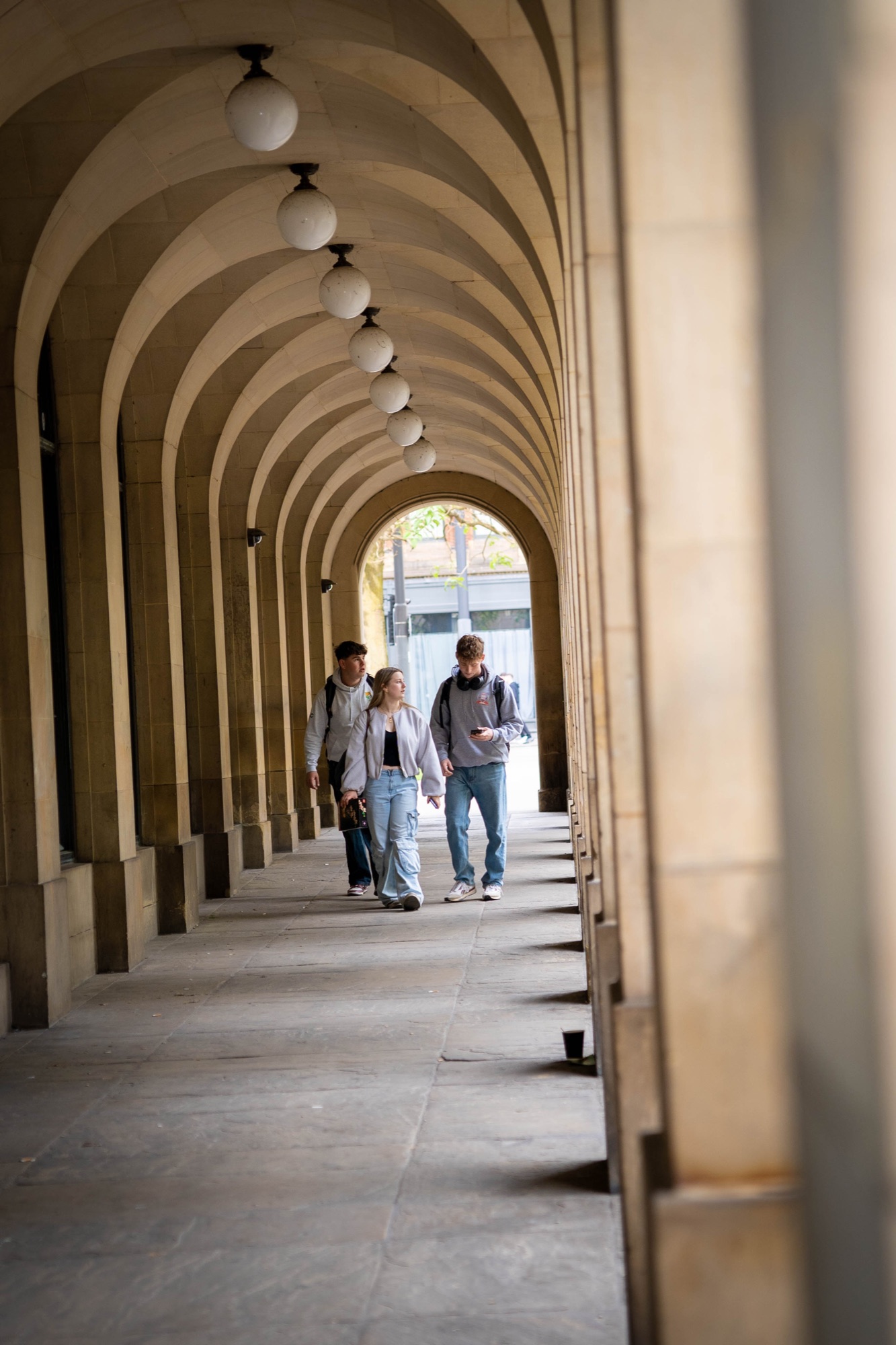 Three friends walking through a vaulted stone arcade